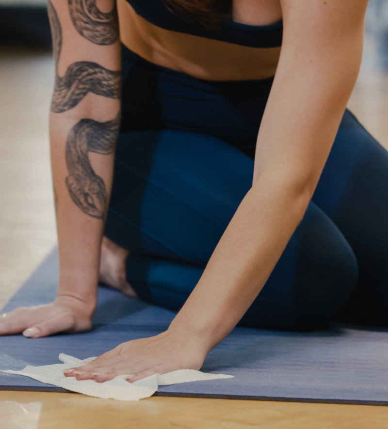Staff member wiping a yoga mat with studio cleaning wipes between classes