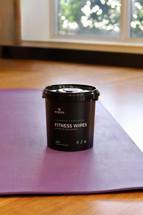 Yoga studio staff member wiping a yoga mat with plant-based cloth wipes between classes